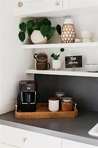 Minimalist kitchen coffee station with plant, mugs, and decor on shelves.