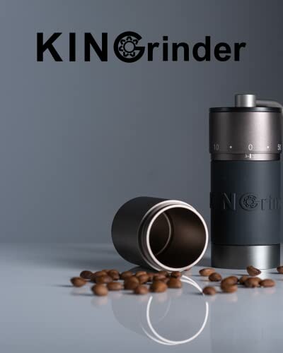 Manual coffee grinder with scattered coffee beans on a reflective surface.